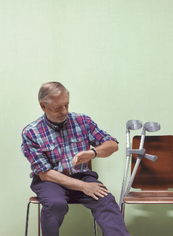 A man sitting in a doctor's waiting room with crutches, looking at his watch